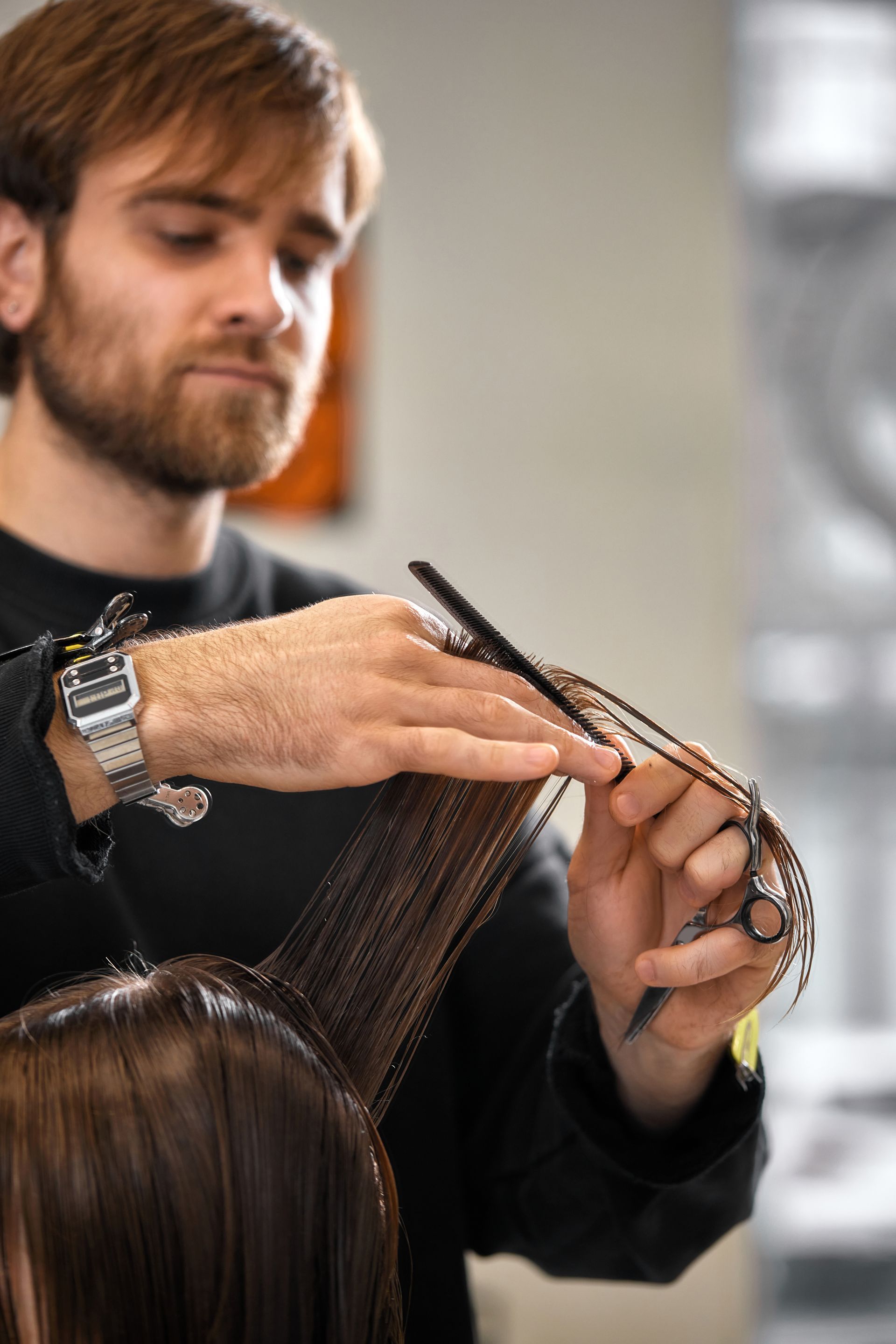 Man cutting a woman's hair in a salon with black scissors and comb.