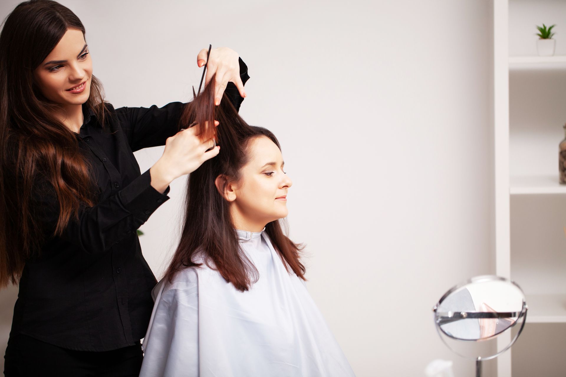 Hairdresser cutting a woman's hair in a salon. The hairdresser is smiling, and the woman is looking down.