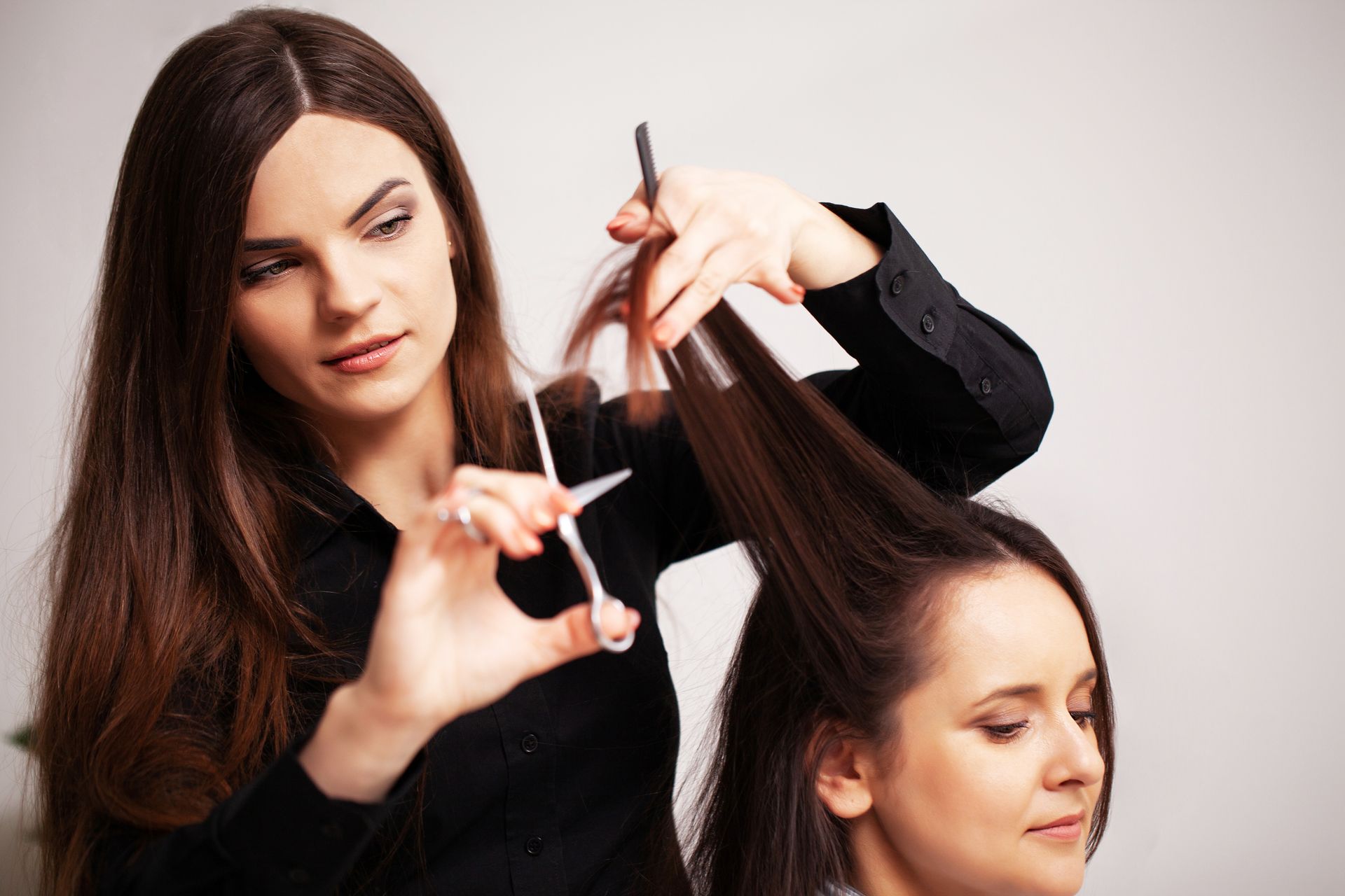 Hairdresser cutting a customer's long brown hair in a salon; both women are focused on the task.