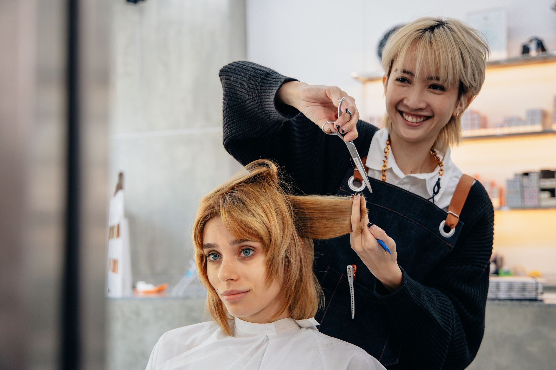 Hairdresser cutting a client's hair in a salon; client is smiling.