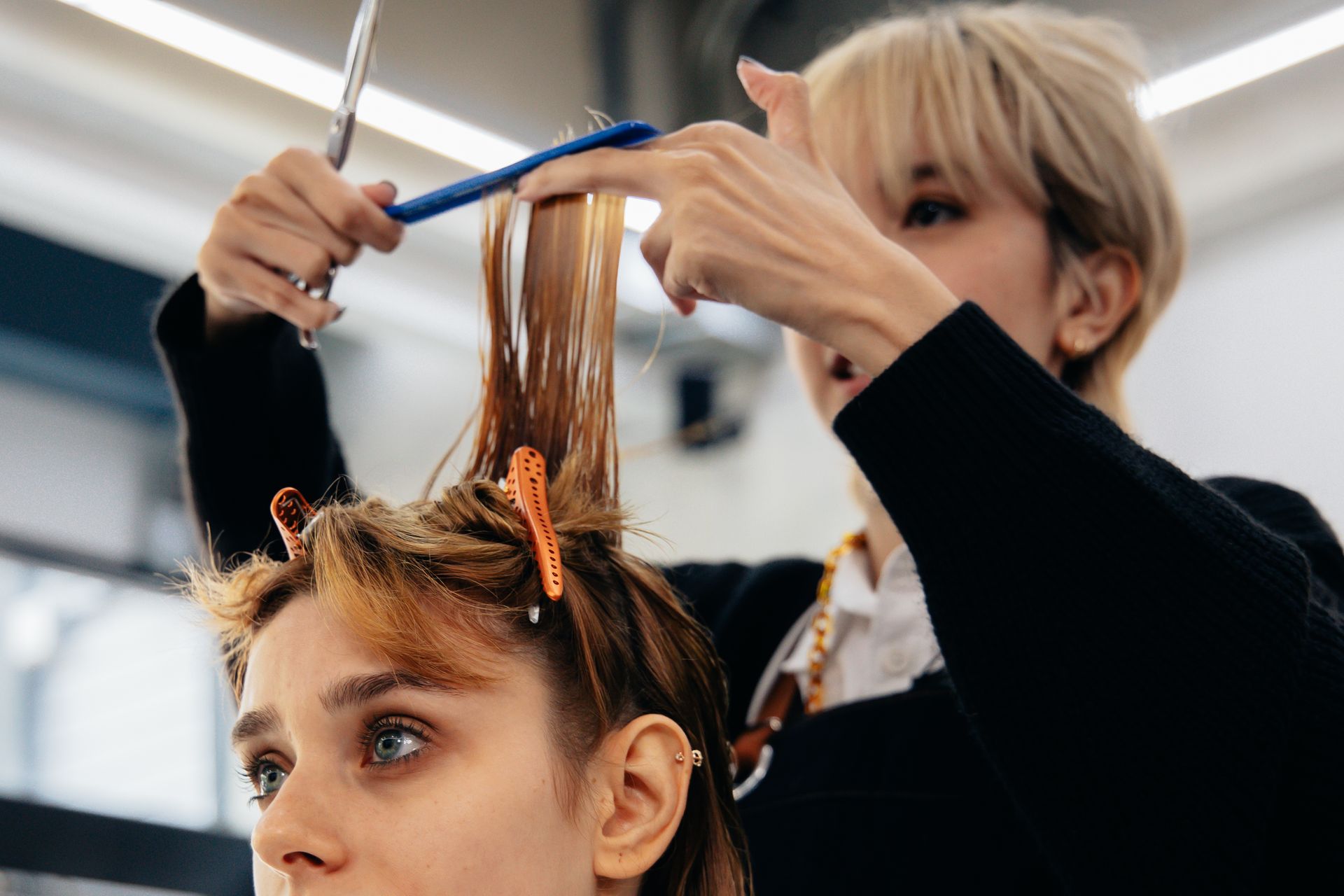Hairdresser cutting client's hair with scissors. Indoor setting. Blondes and blue eyes.