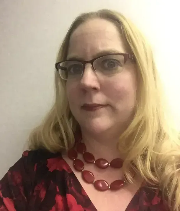 A woman wearing glasses and a red necklace is taking a selfie.