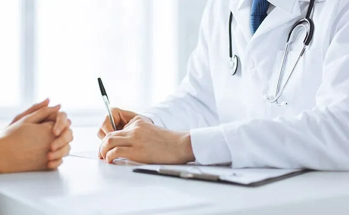 A doctor is sitting at a desk talking to a patient.