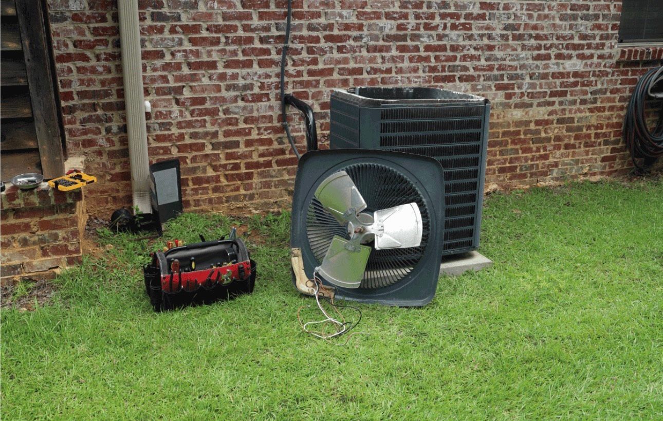 A fan is sitting in the grass next to a brick wall.