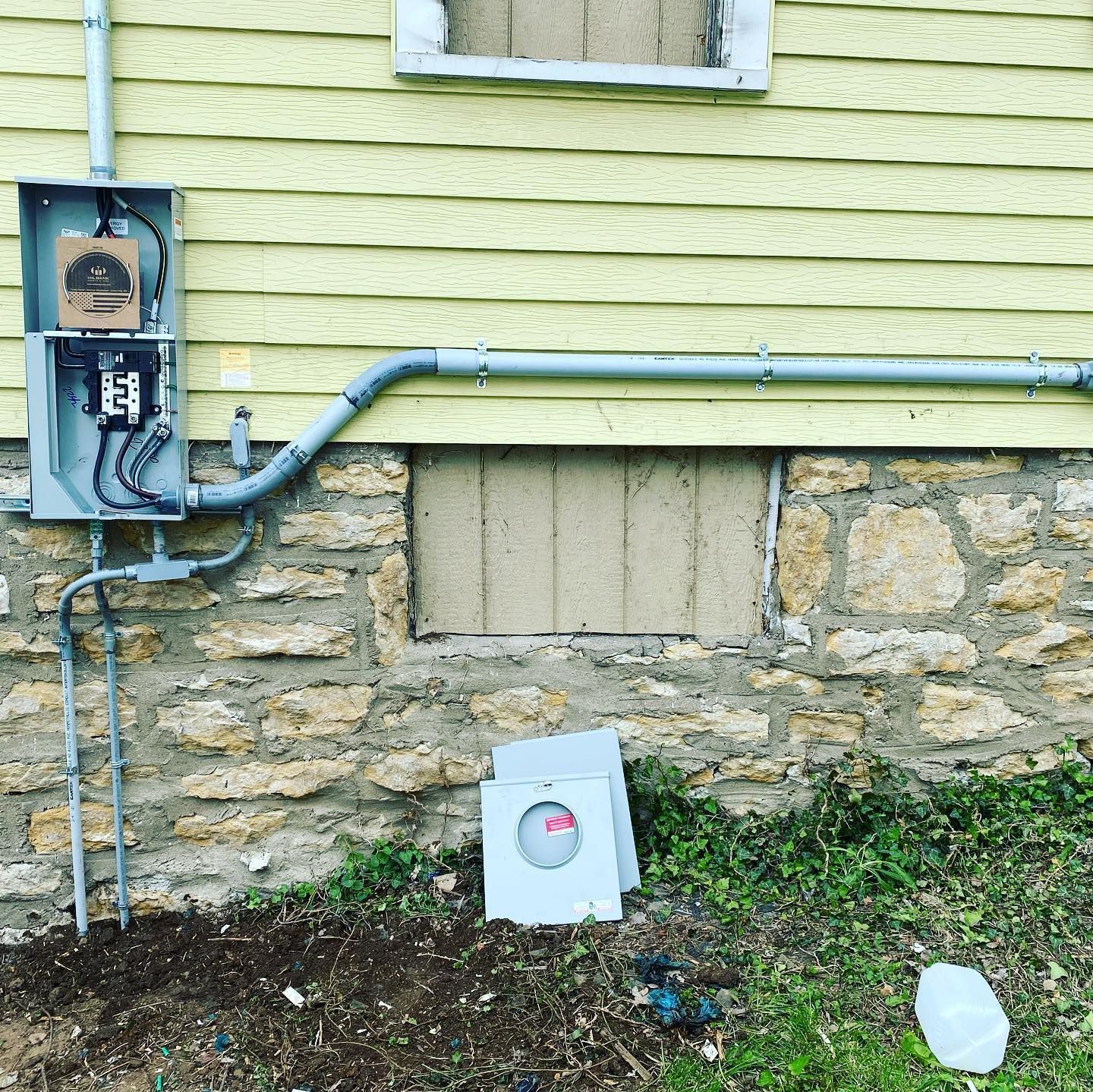 An electrical box is attached to the side of a house.