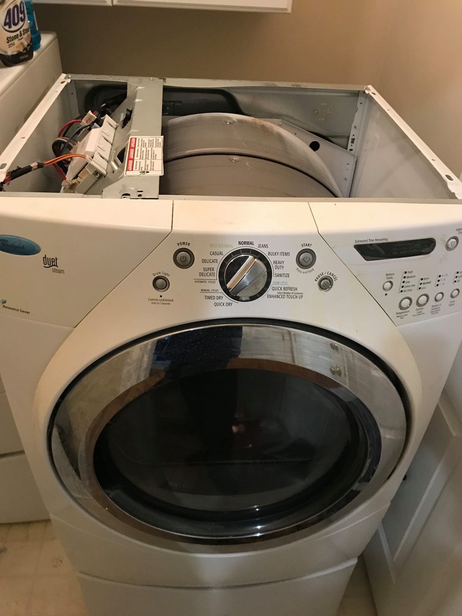 A white washing machine is sitting on the floor in a laundry room.
