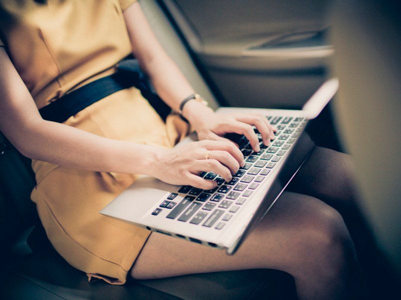 a lady sitting on a car and typing on her laptop