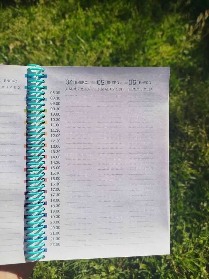 Cuaderno abierto con lista, encuadernación en espiral color turquesa, al aire libre sobre césped verde.