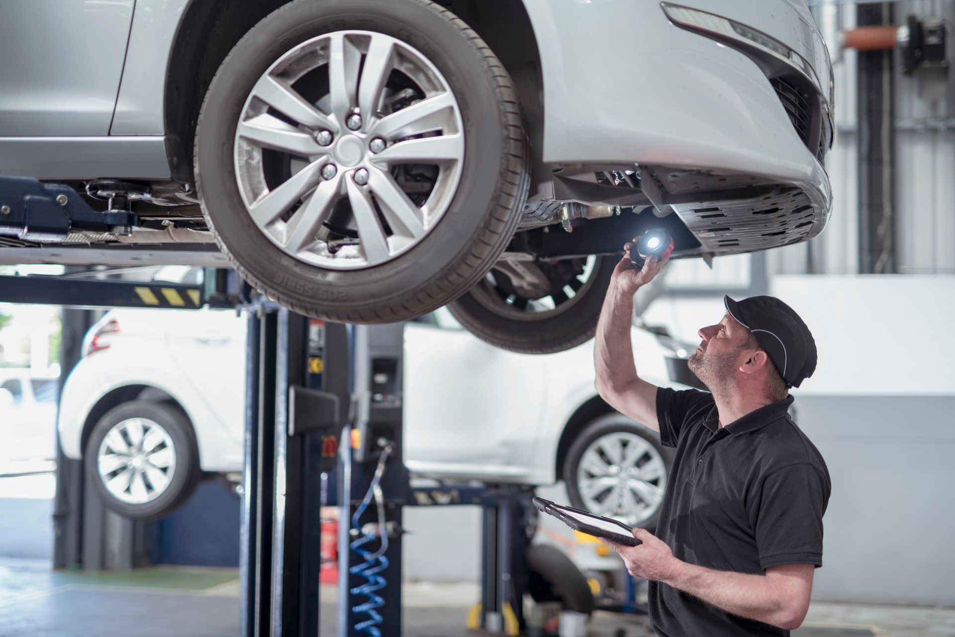 Automotive repair technician inspecting car on lift in service center garage for maintenance check.