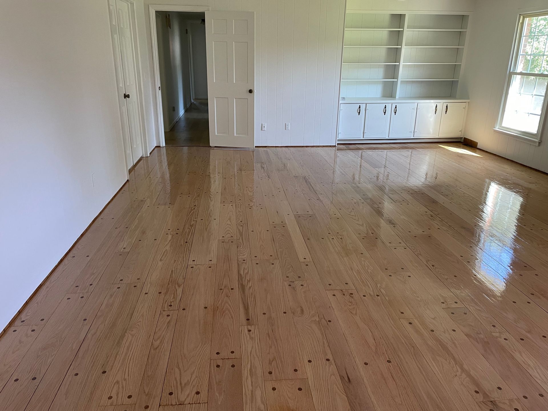 An empty living room with hardwood floors and white walls.