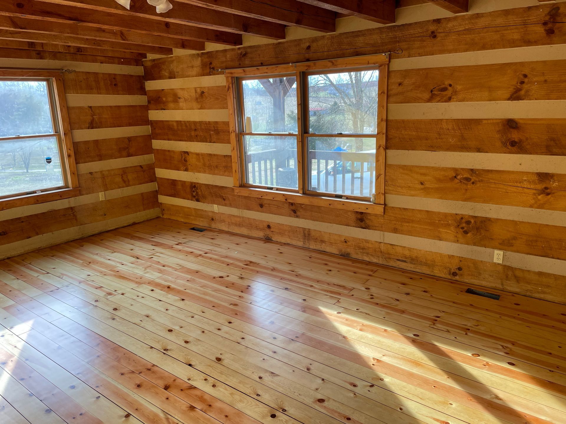 An empty room in a log cabin with wooden floors and windows.