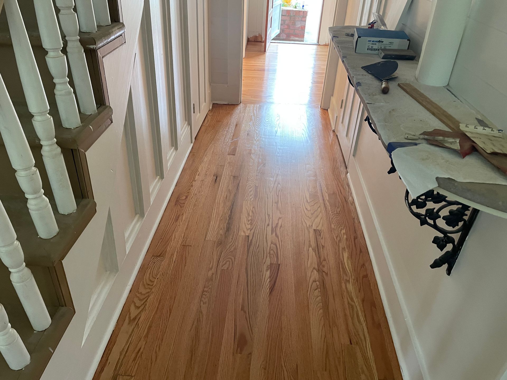 A hallway with hardwood floors and white stairs.