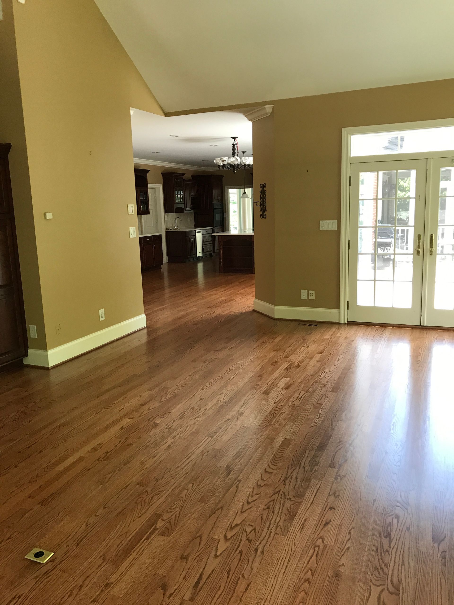 An empty living room with hardwood floors and a kitchen in the background.