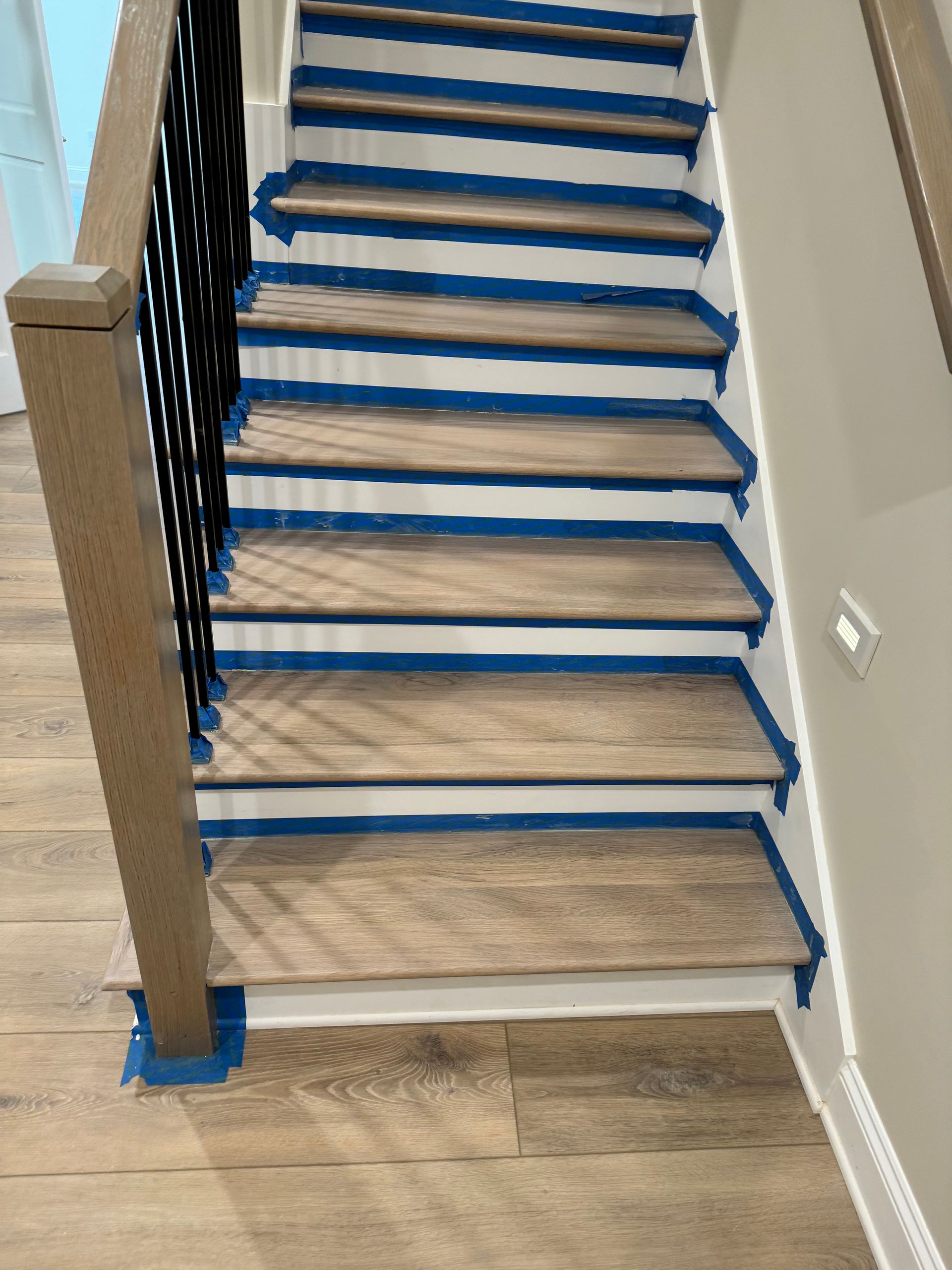 A wooden staircase with blue tape on the steps is being painted.