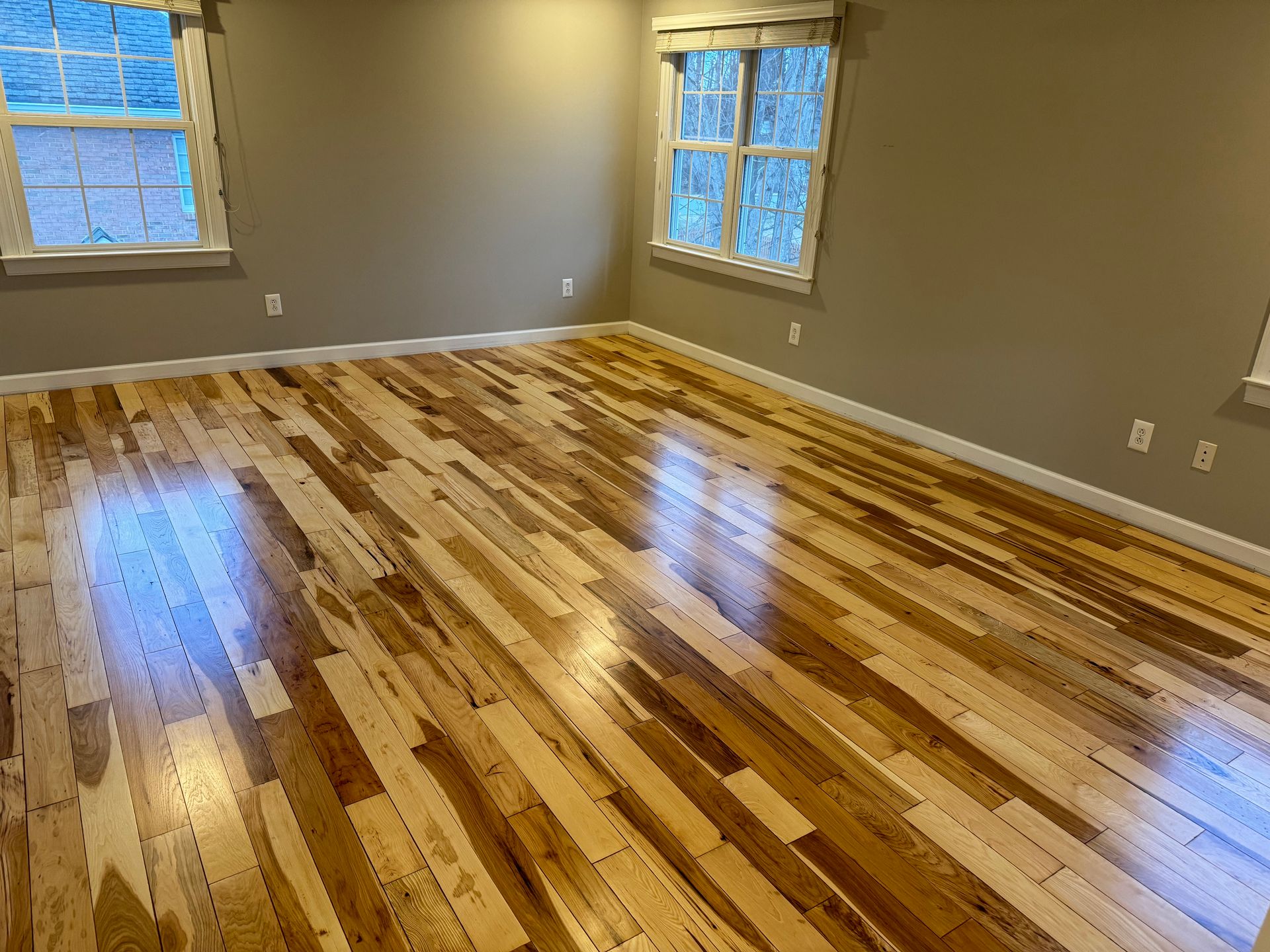 An empty room with hardwood floors and two windows.