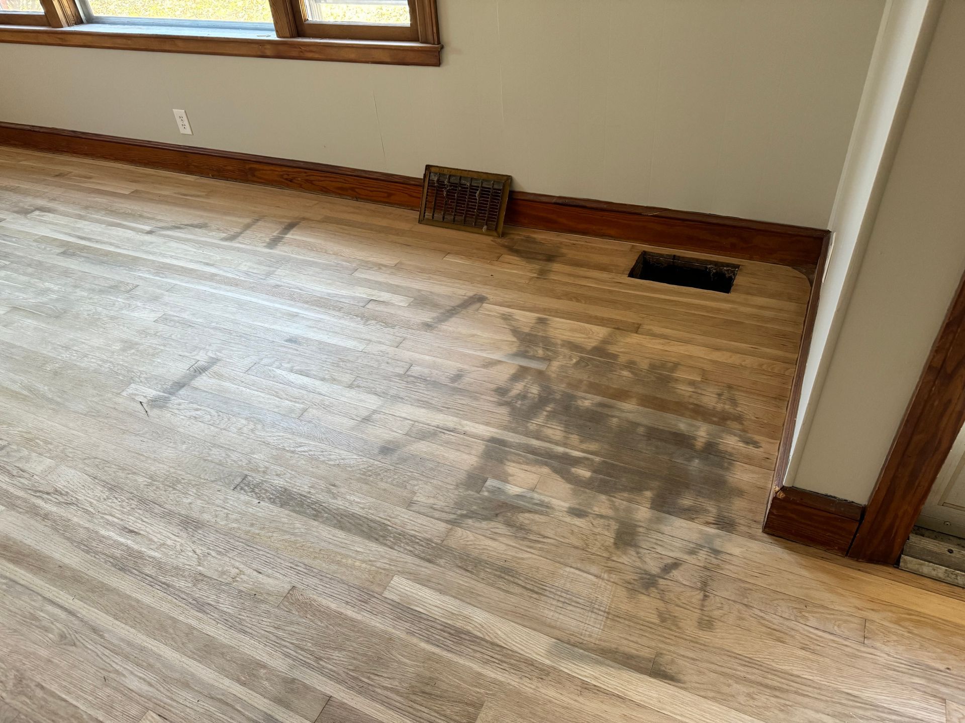 A wooden floor in a room with a window and a vent.