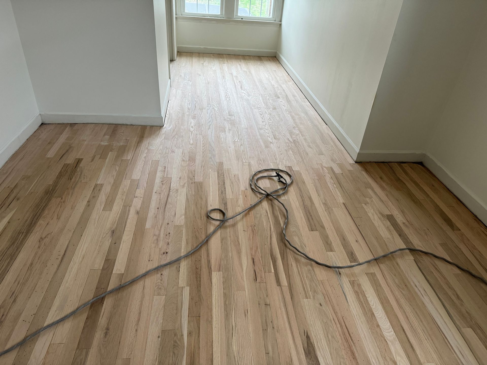 A wooden floor with a cord laying on it in a room.
