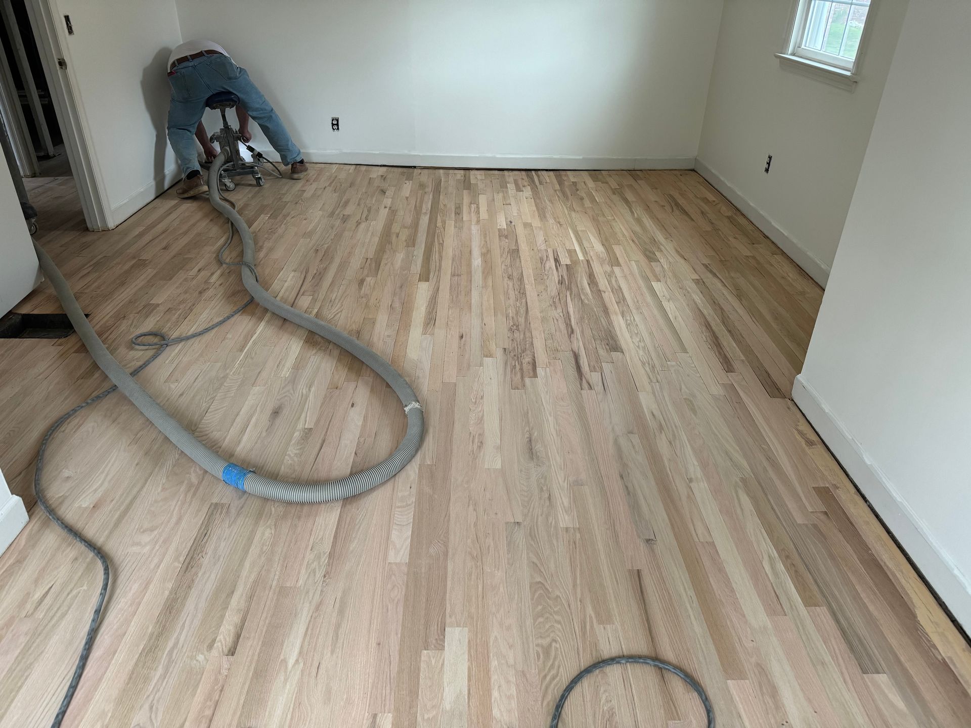 A man is working on a wooden floor with a vacuum cleaner.