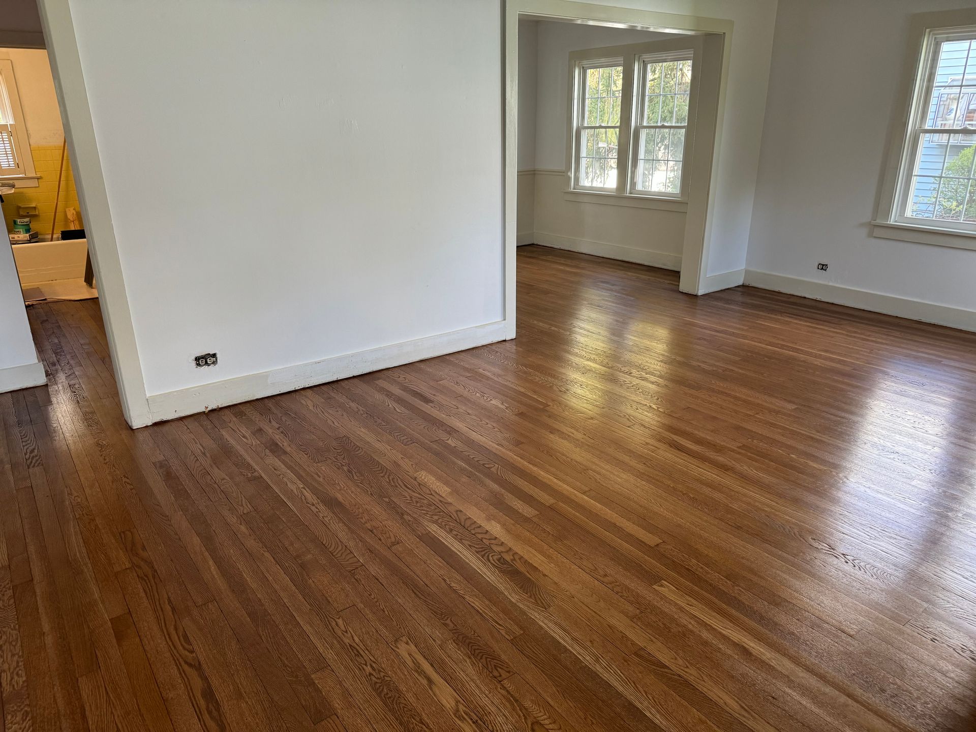 An empty living room with hardwood floors and white walls.