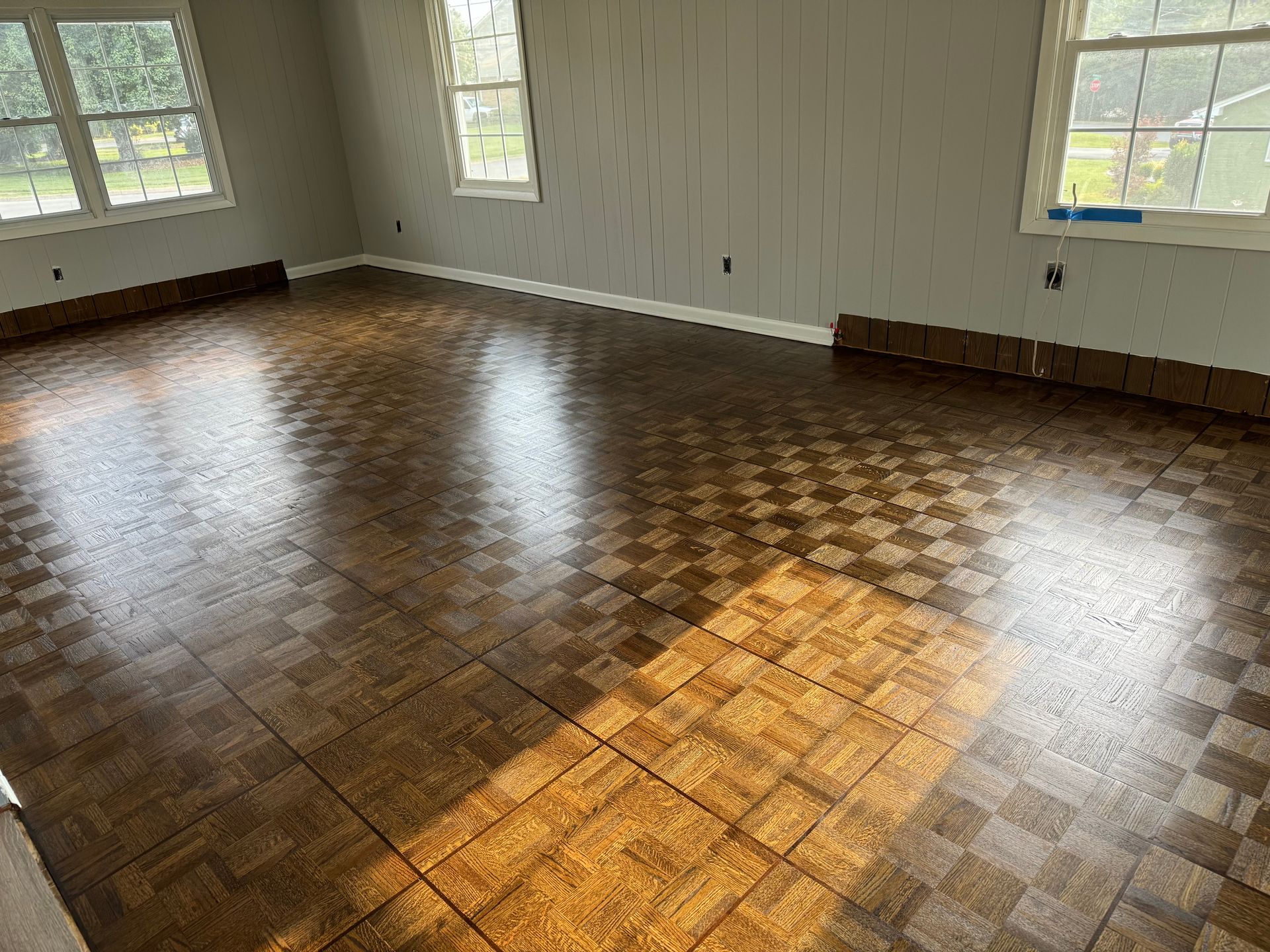 A large empty room with a wooden floor and windows.