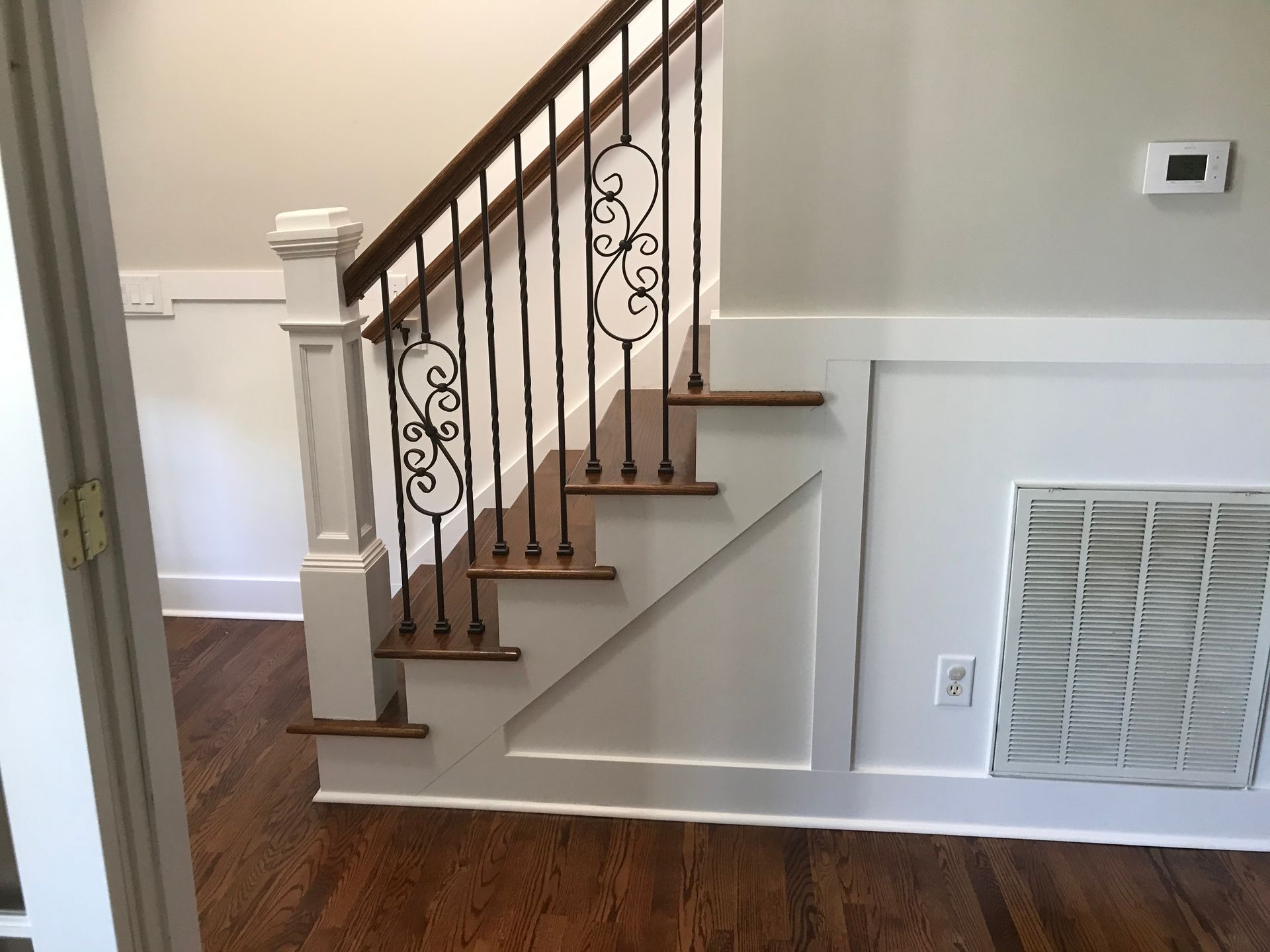 A staircase with a wrought iron railing is in a room with hardwood floors.