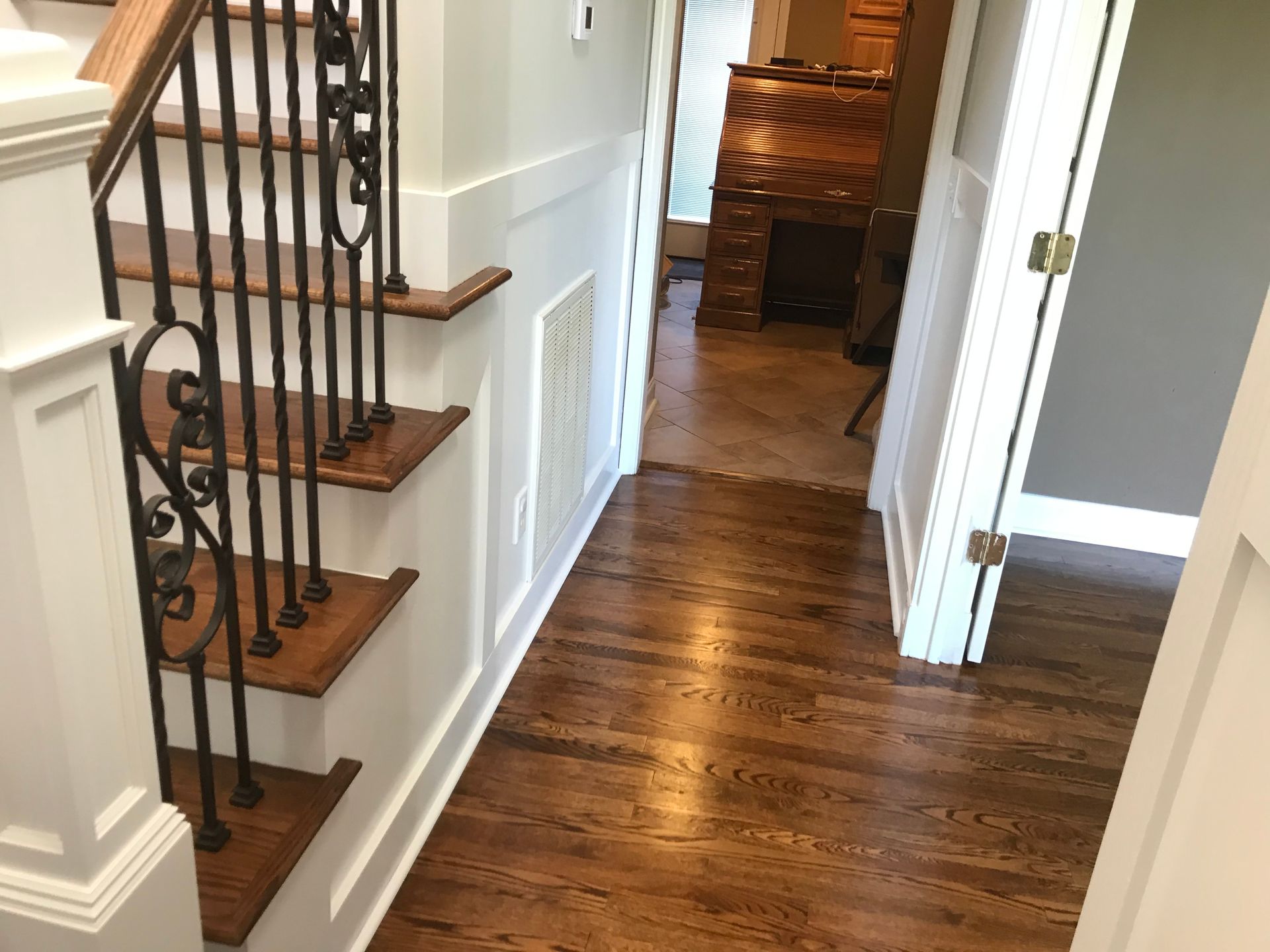 A hallway with wooden stairs and a wrought iron railing