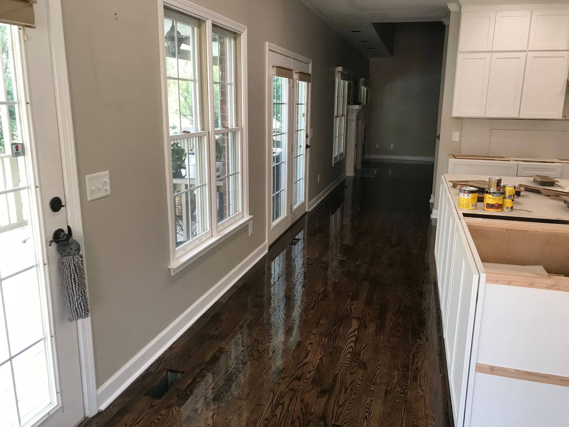 A long hallway leading to a kitchen with hardwood floors and white cabinets.