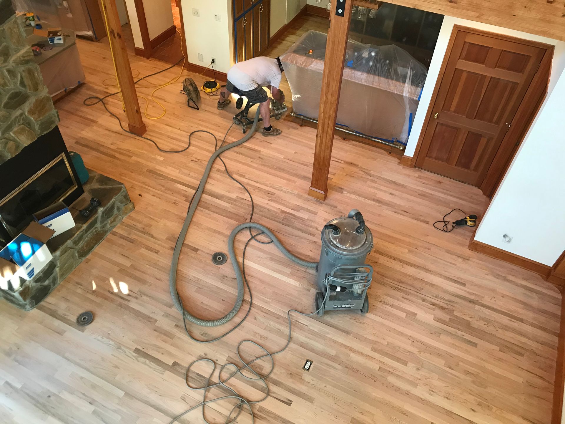 A man is using a vacuum cleaner to clean a wooden floor in a living room.