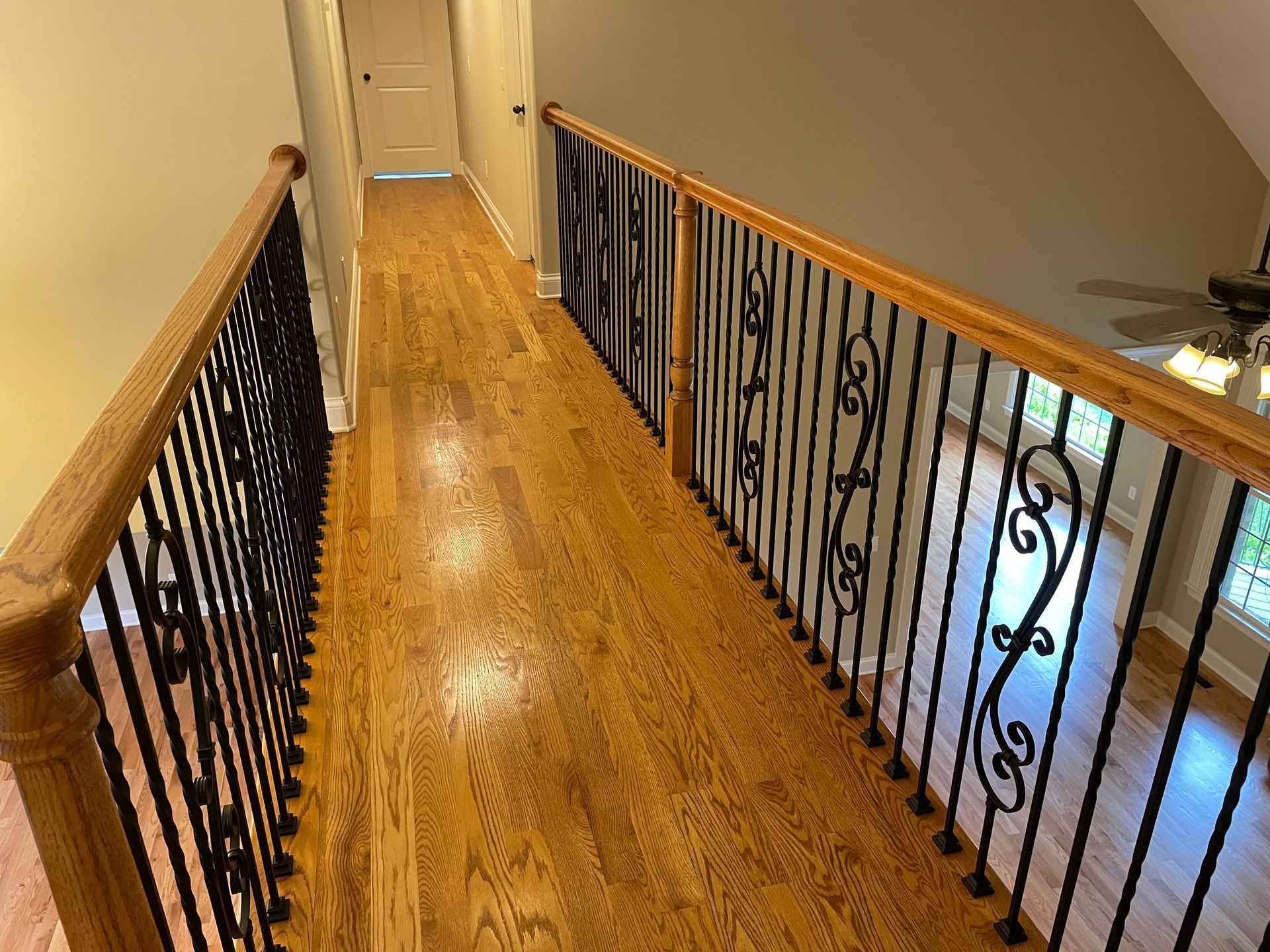 A hallway with hardwood floors and a wrought iron railing.