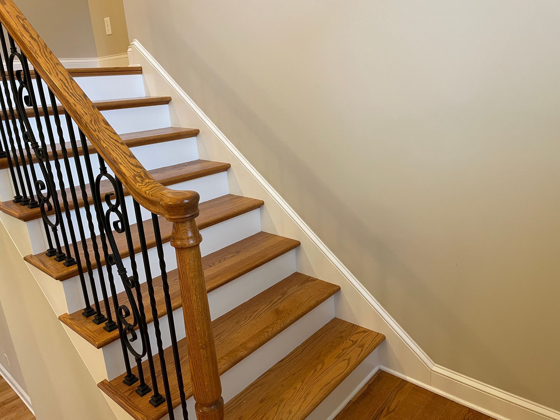 A wooden staircase with white steps and a wrought iron railing.