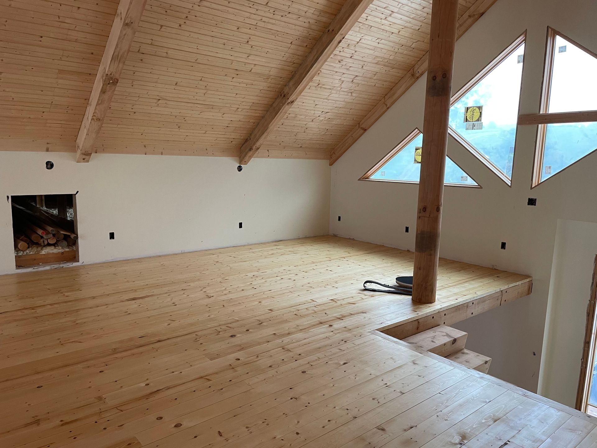 An empty room with a wooden floor and a triangle window