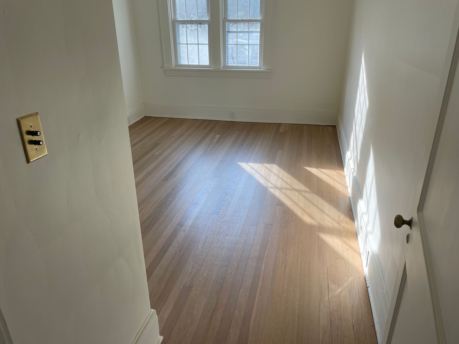 An empty room with hardwood floors and two windows.