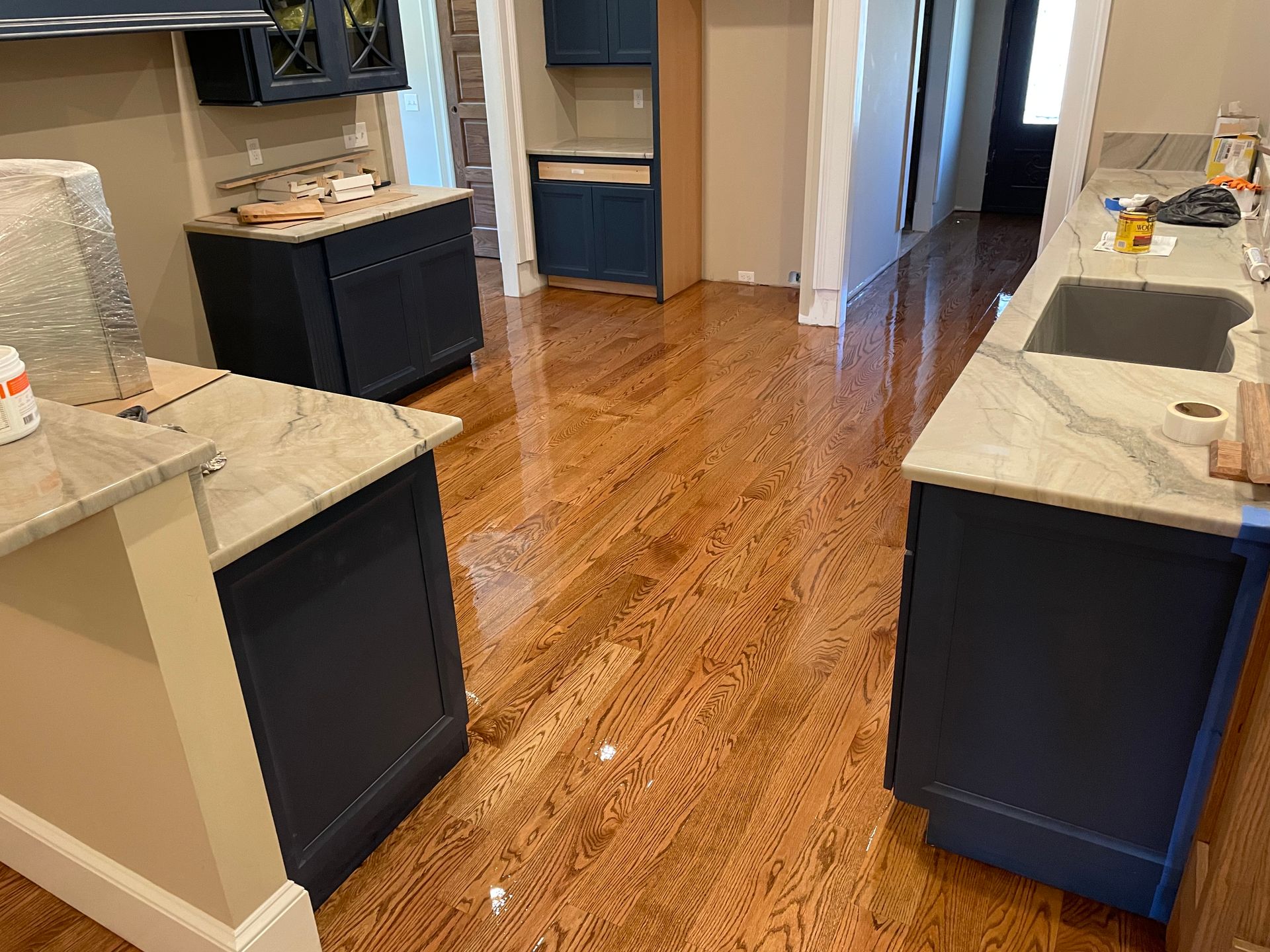 A kitchen with hardwood floors , blue cabinets , white counter tops and a sink.