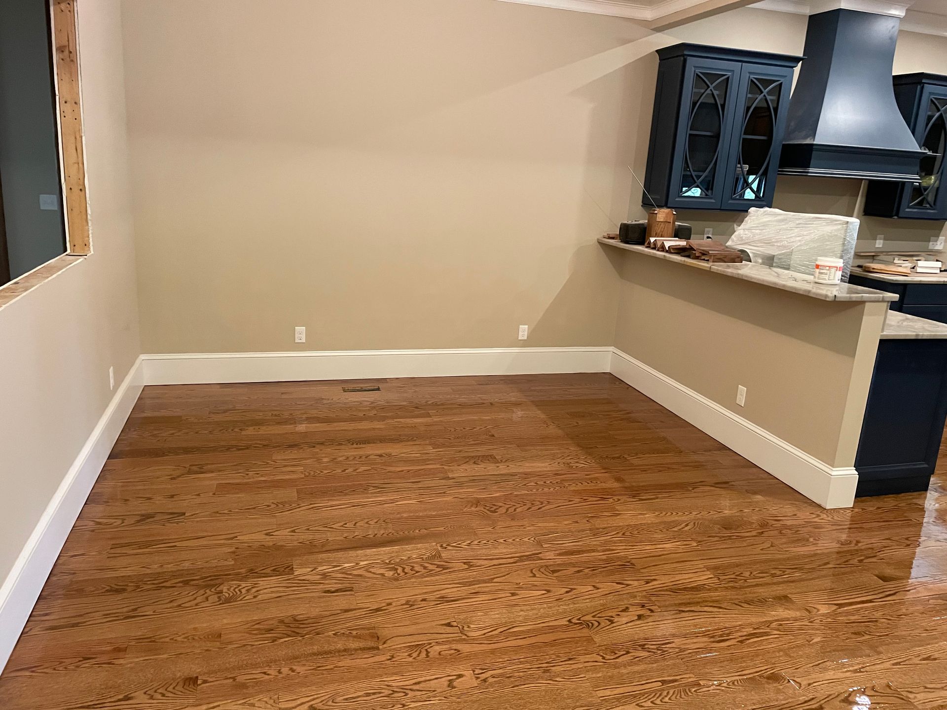 An empty room with hardwood floors and a kitchen in the background.
