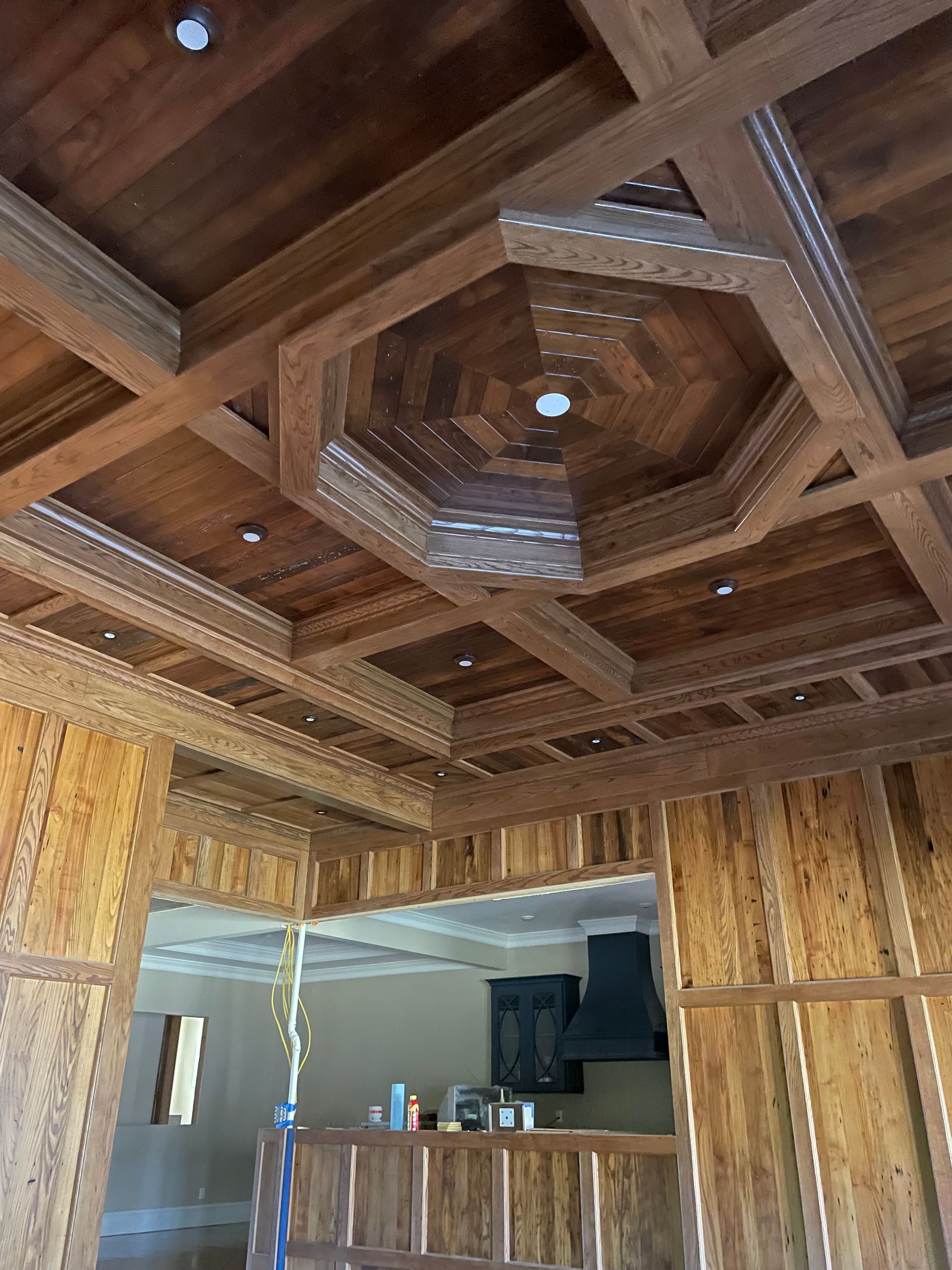 A wooden ceiling in a room with a kitchen in the background.
