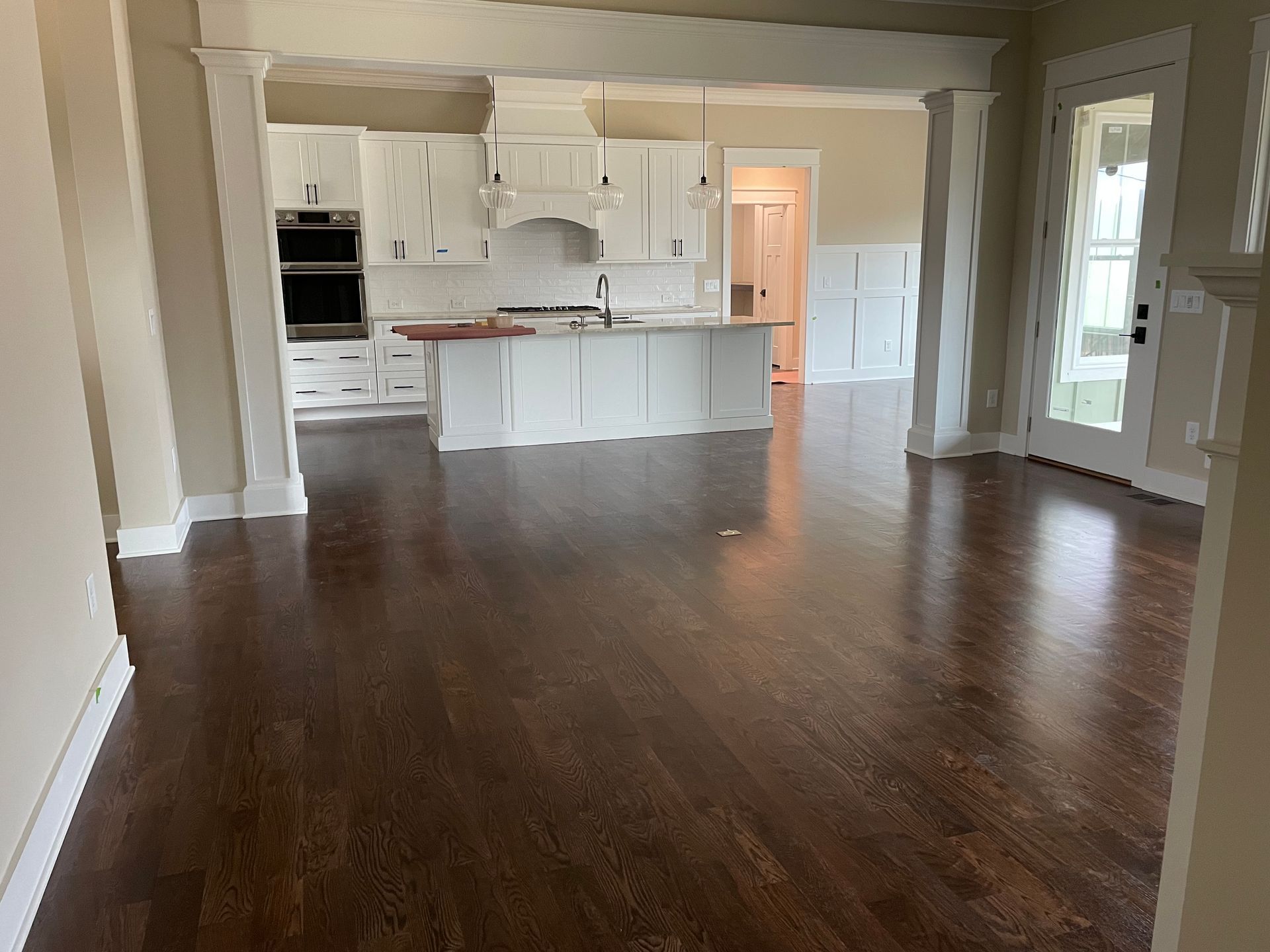 An empty living room with hardwood floors and a kitchen in the background.
