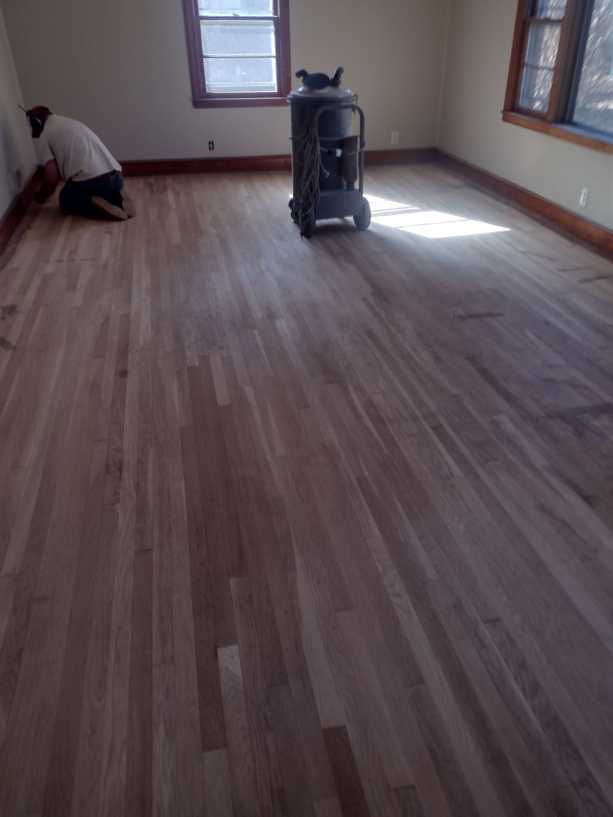 A man is kneeling on a wooden floor in a room
