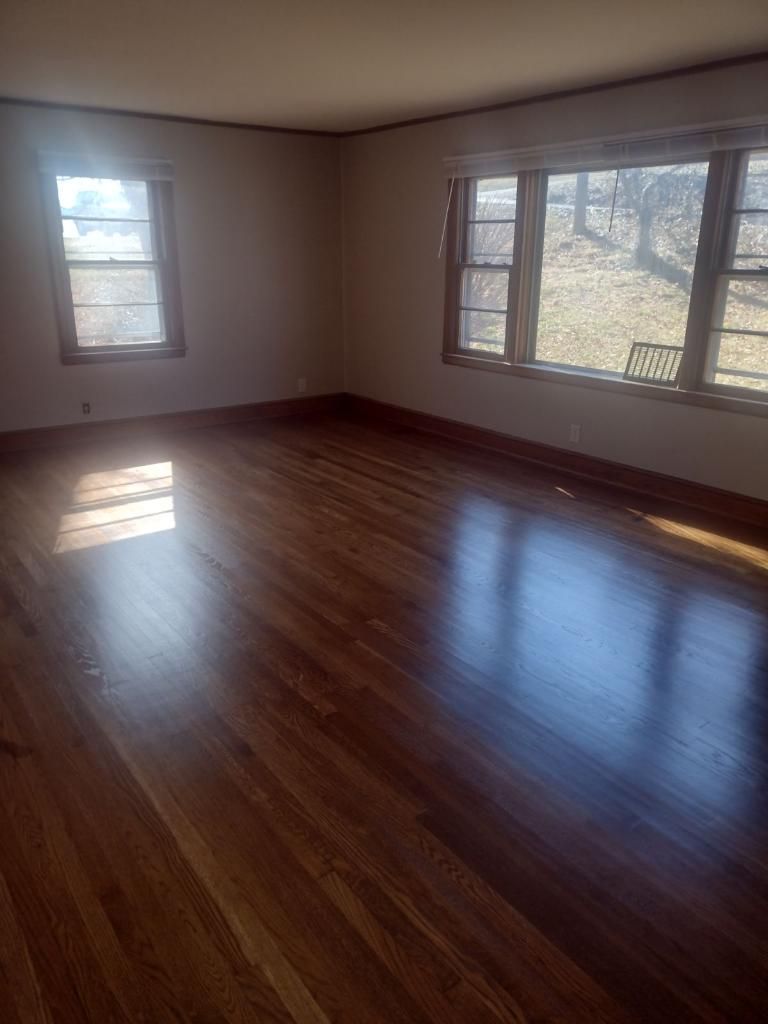 An empty living room with hardwood floors and two windows.