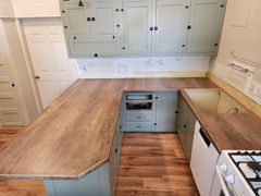 Kitchen with sage green cabinets and wood-look countertops. The room has a U-shape layout, a white dishwasher, and a gas stove.