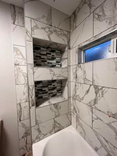 Bathroom with white marble-patterned tiles. Two recessed shelves with mosaic tile backs are in the shower wall. A small window is on the right.