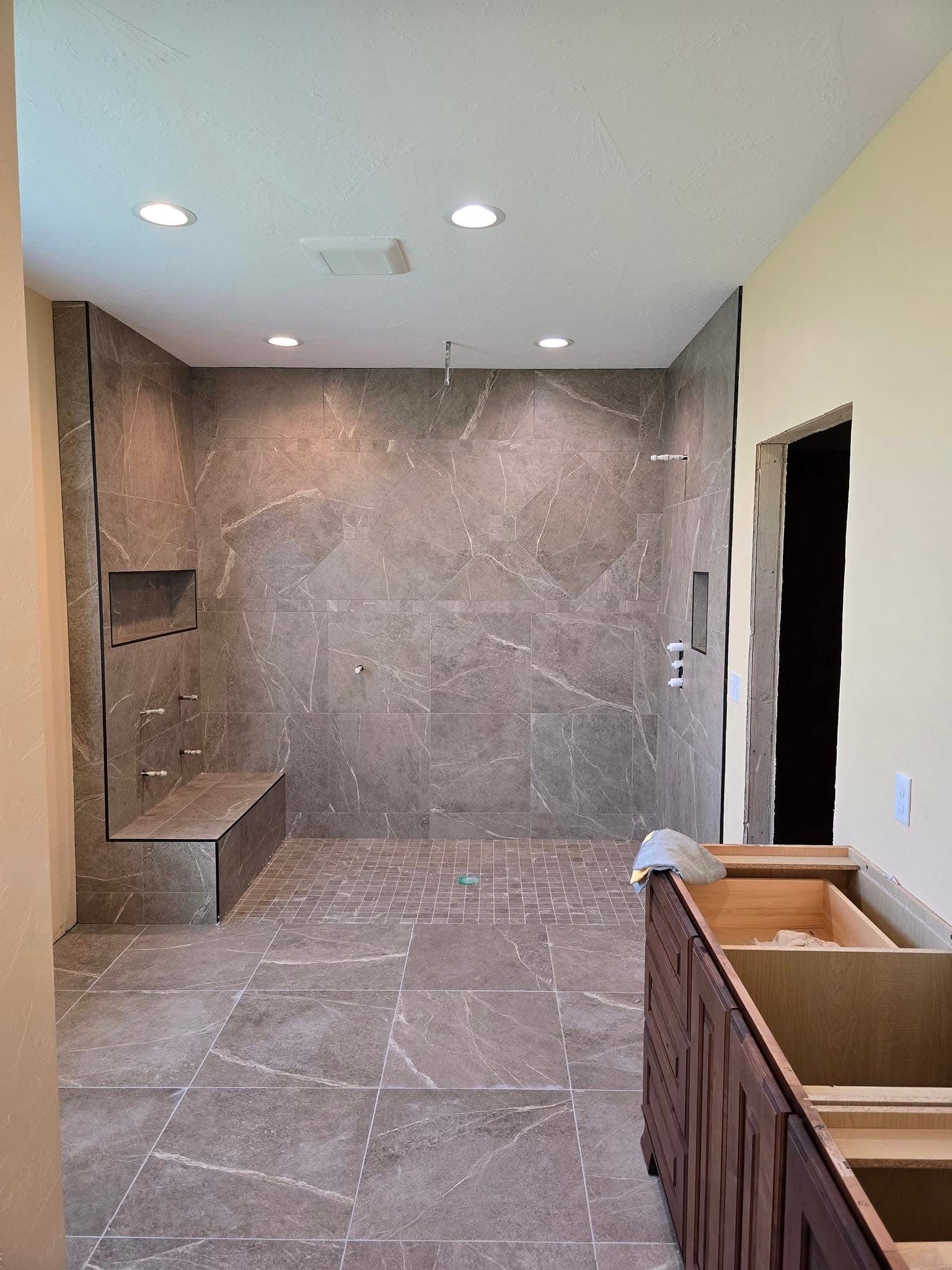 Bathroom with a large tiled shower, built-in bench, and vanity under construction; earth-toned colors.