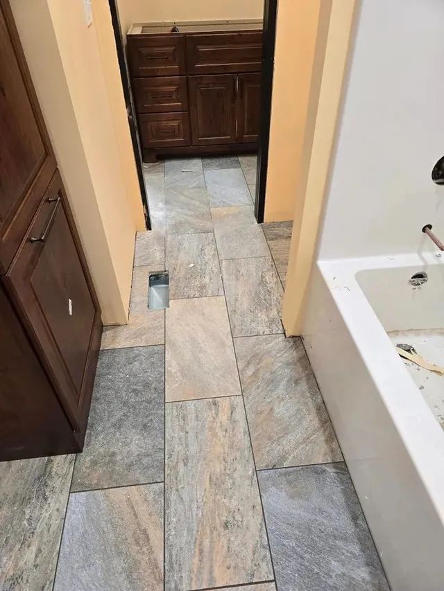Bathroom hallway with gray and beige tile flooring, dark brown cabinets, and a white bathtub.