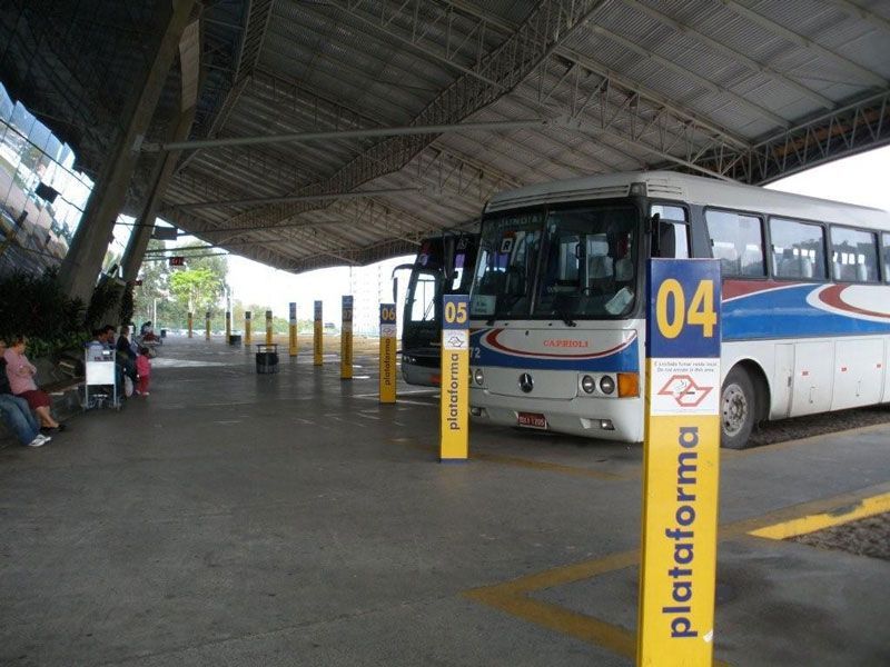 Homem na sala de controle falando ao telefone, supervisionando ônibus estacionados ao ar livre sob abrigo.