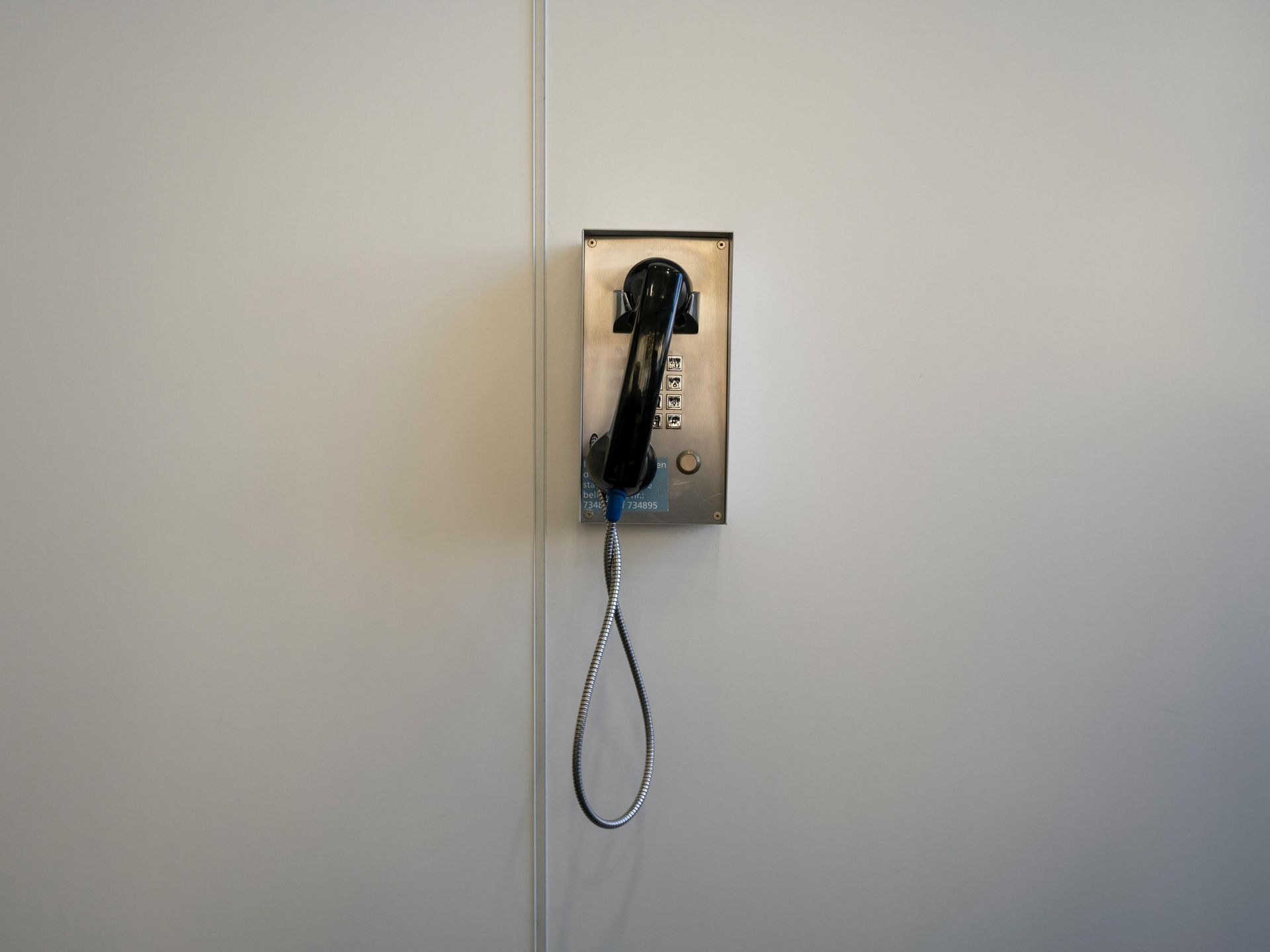 Telefone público em uma parede clara, fone abaixado. Prateado e preto.