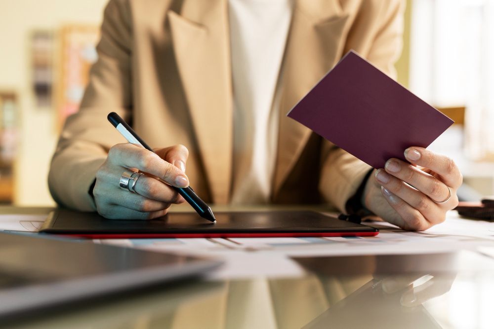 Una mujer está sentada en un escritorio sosteniendo un pasaporte y un bolígrafo.