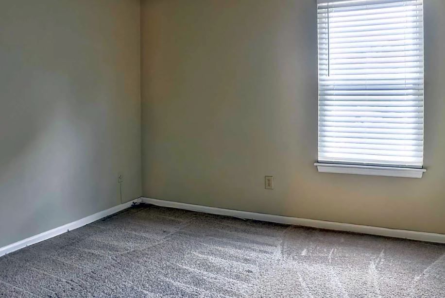 An empty bedroom with a window and blinds.
