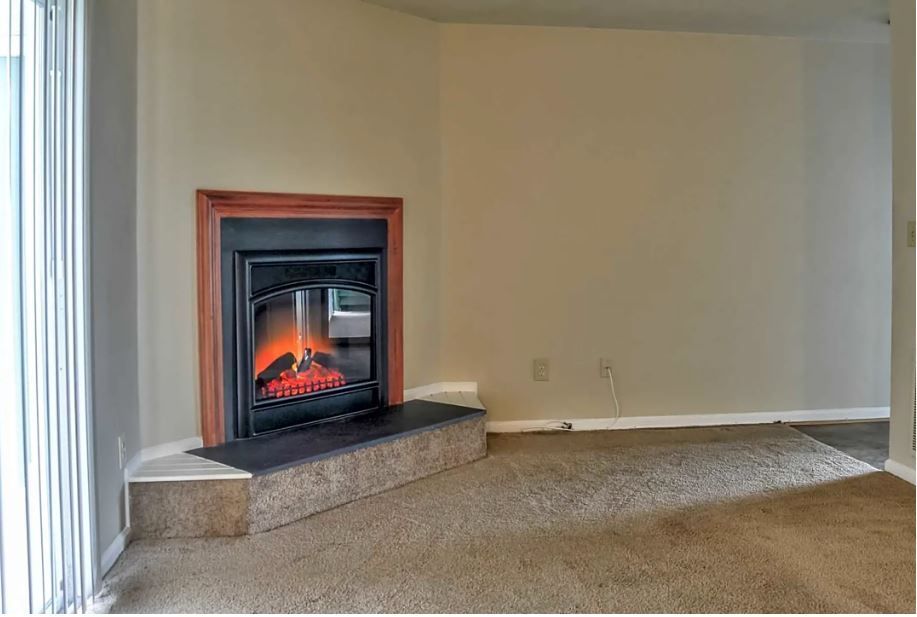 An empty living room with a fireplace in the corner