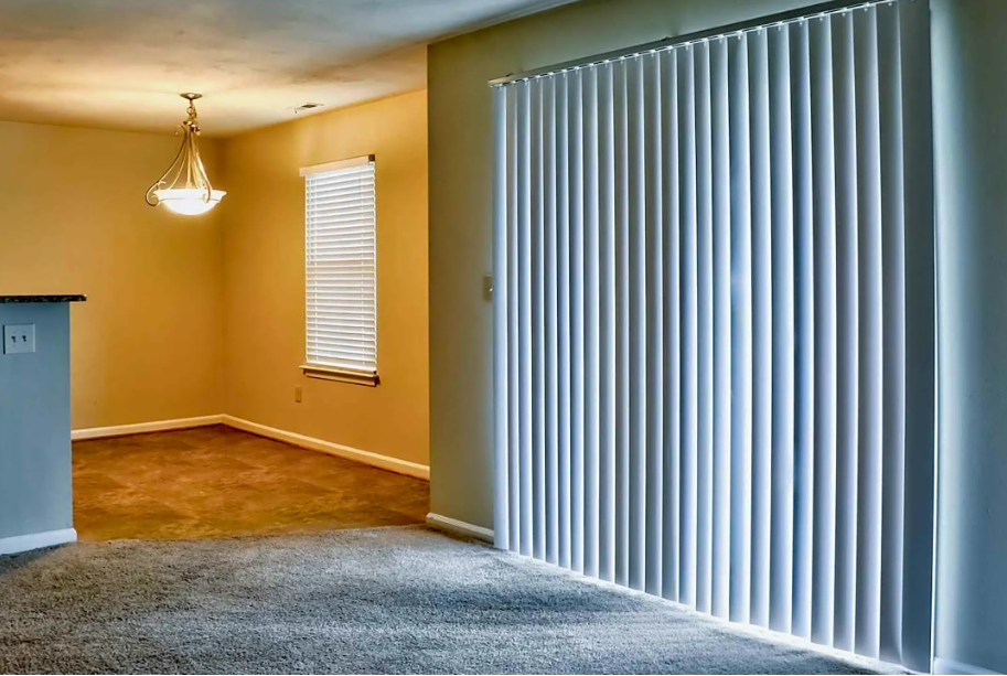 A living room with a sliding glass door and white blinds.