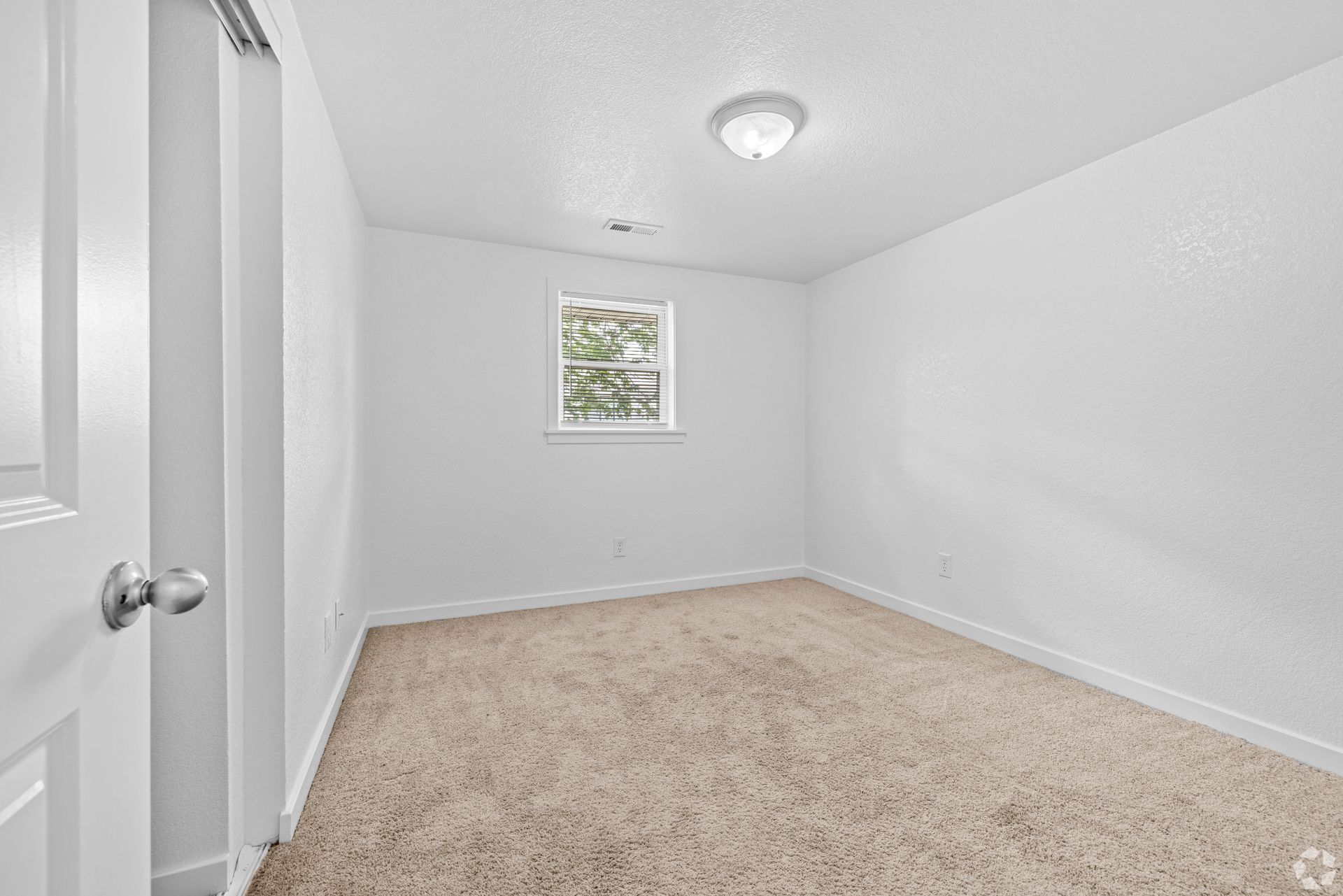An empty bedroom with a window and a carpeted floor.