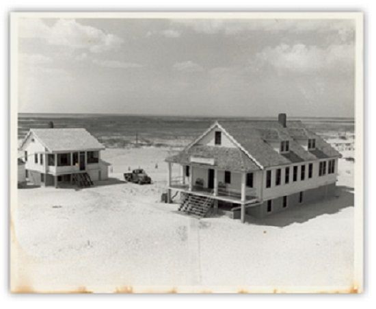 A black and white photo of two houses on the beach